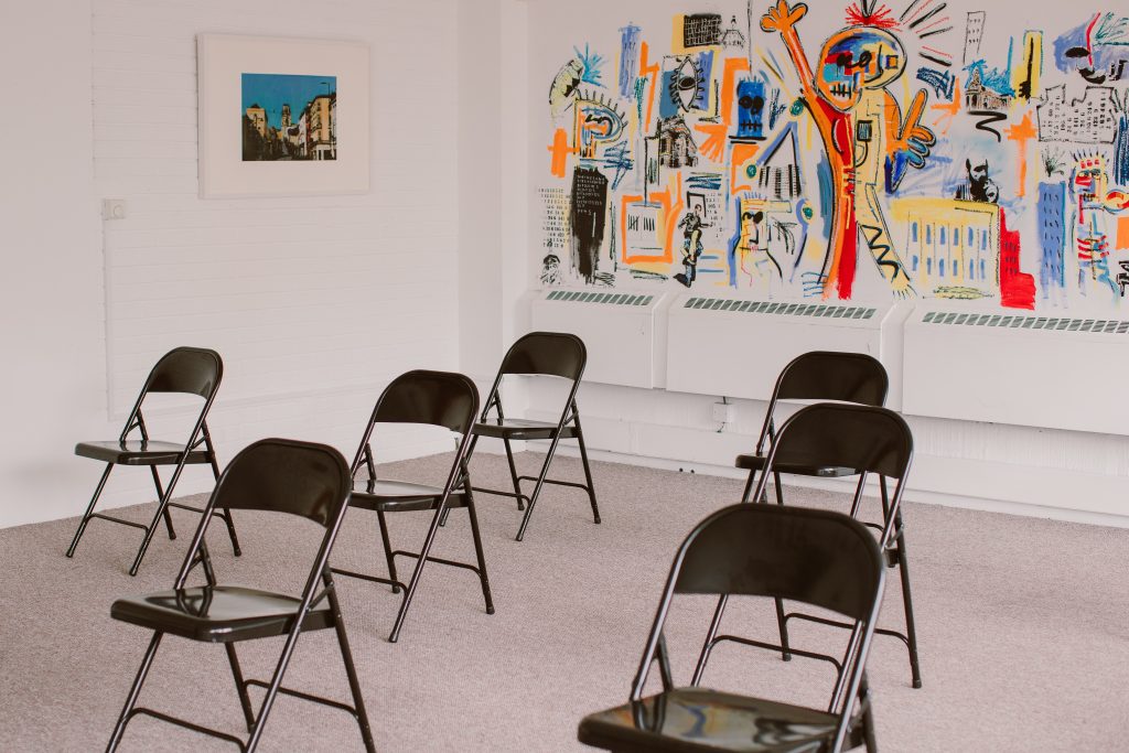 A light room with a painting on the wall and fold out chairs arranged neatly