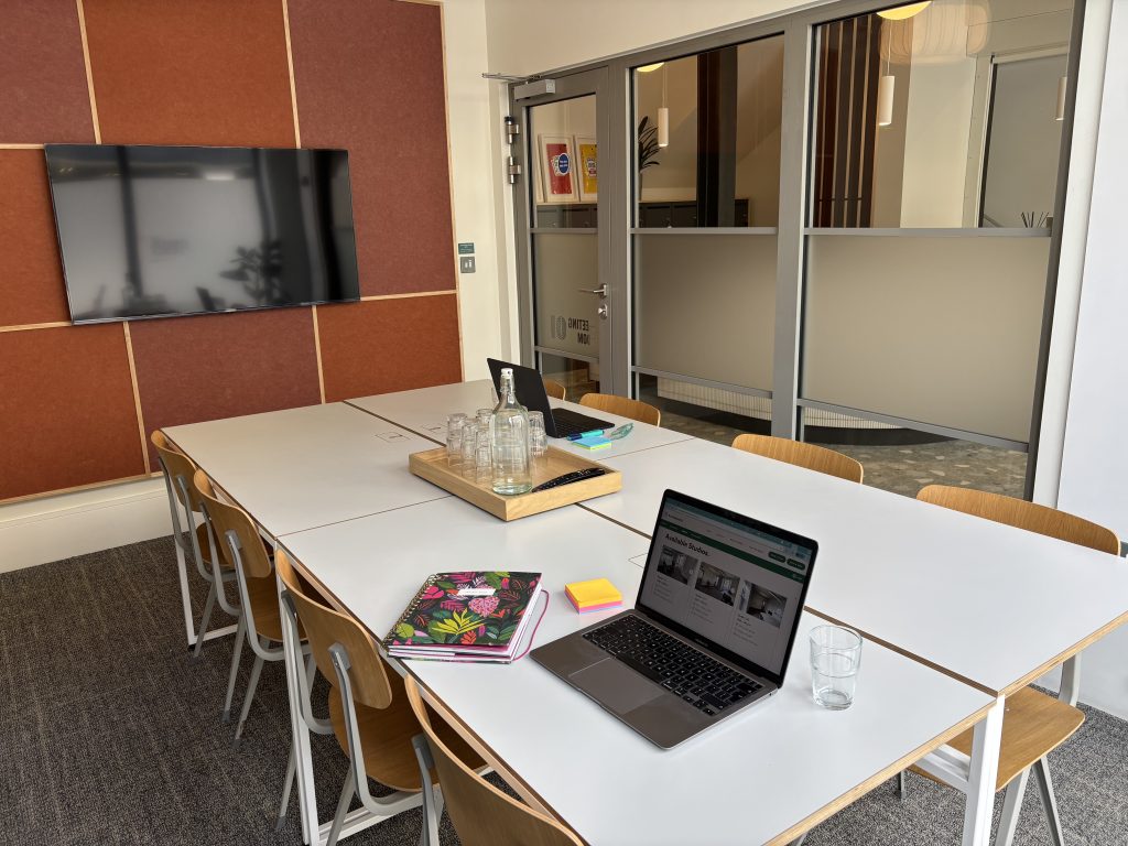A meeting room with a table, chairs, laptop and TV screen.